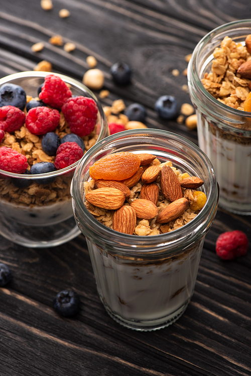 closeup of delicious granola with berries, dried apricots, nuts and yogurt in glass cups on wooden surface