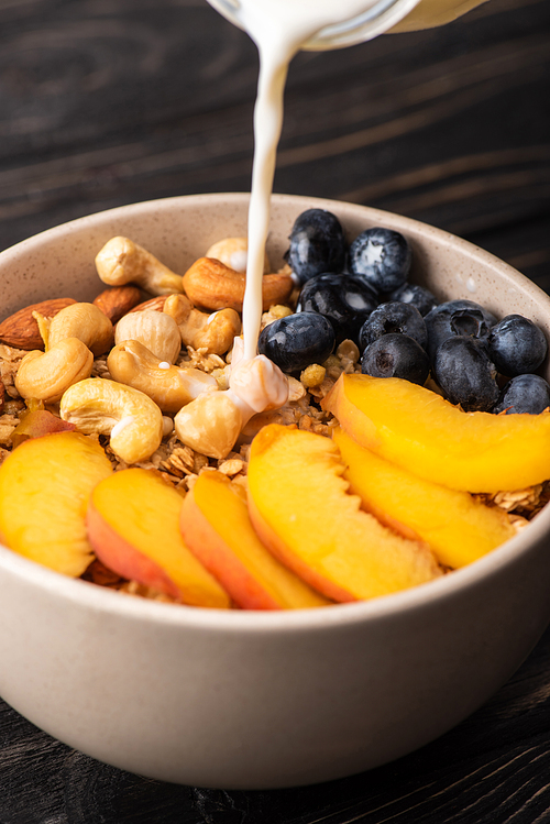 yogurt pouring on delicious granola with nuts, peach, blueberry in bowl