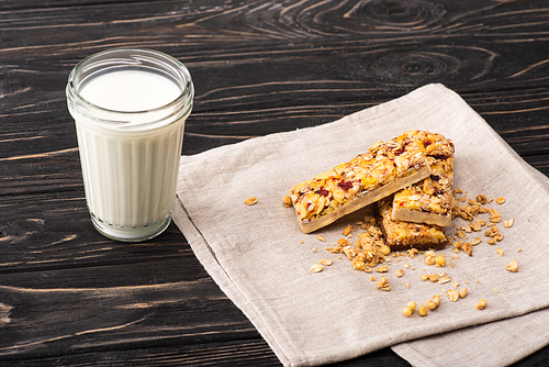 delicious muesli bars on napkin near glass of milk on wooden surface