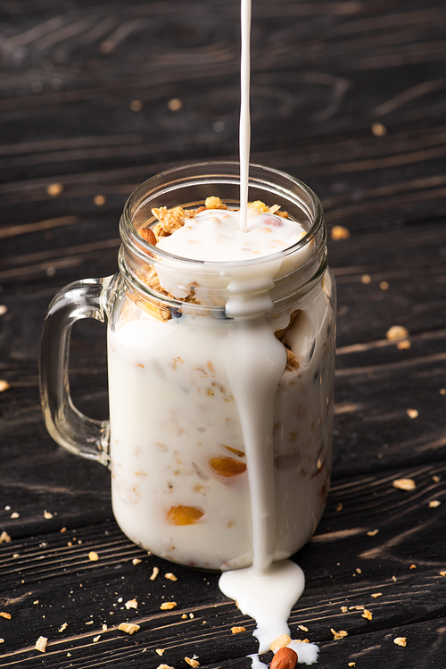 delicious granola with pouring yogurt in glass jar