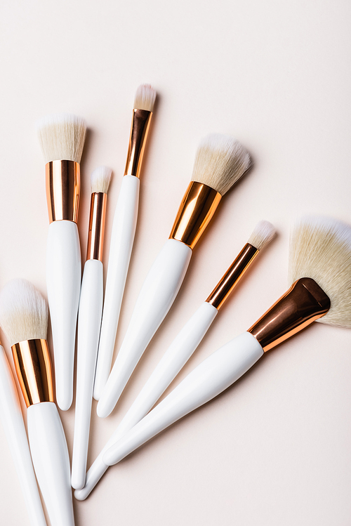 top view of white and golden cosmetic brushes set on beige background