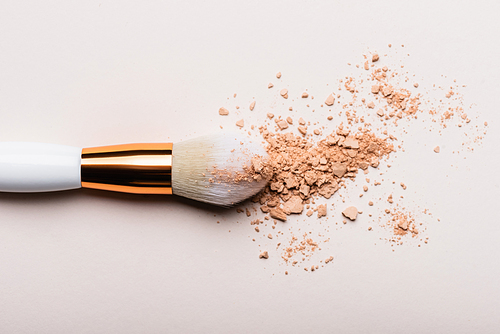 top view of cosmetic brush with face powder on beige background