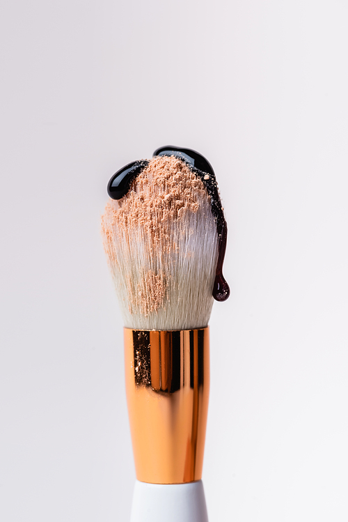 close up view of cosmetic brush with face powder and dripping black liquid isolated on white