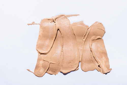 top view of beige face foundation brushstrokes on white background