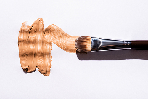 top view of cosmetic brush with face foundation brushstrokes on white