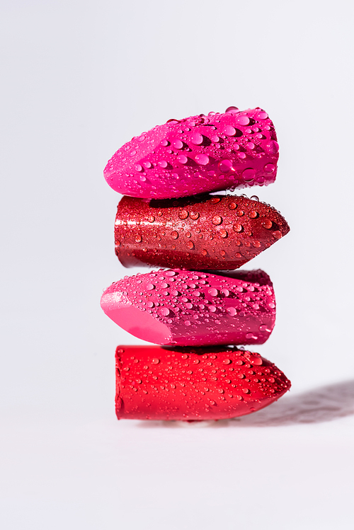 close up view of wet colorful lipsticks on white background