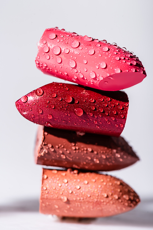 close up view of wet colorful lipsticks on white background