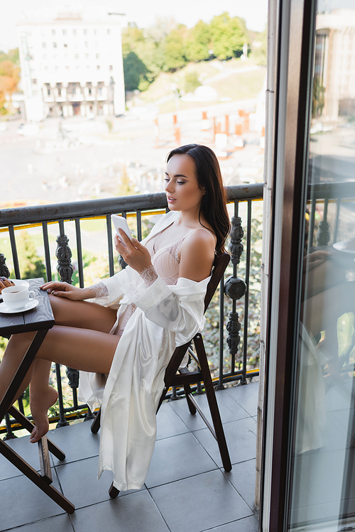brunette woman sitting on balcony and holding smartphone