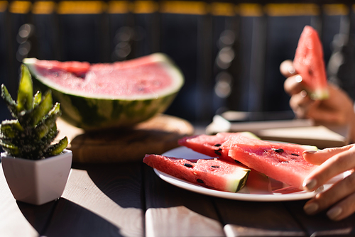 cropped view of woman eating watermelon on balcony and plate with watermelon slices on foreground