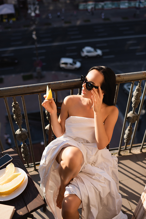 sexy brunette woman in sunglasses and covered in white sheet eating balcony