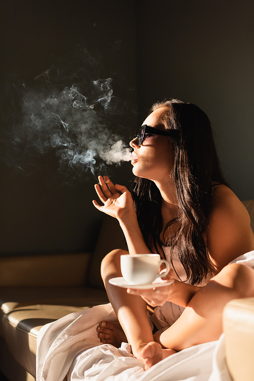 sexy brunette woman covered in white sheet smoking cigarette and drinking coffee