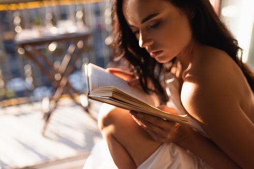 attractive woman covered in white sheet reading book and sitting on balcony