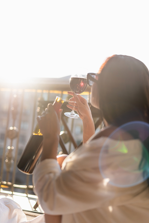 brunette woman in sunglasses and white shirt drinking wine on balcony
