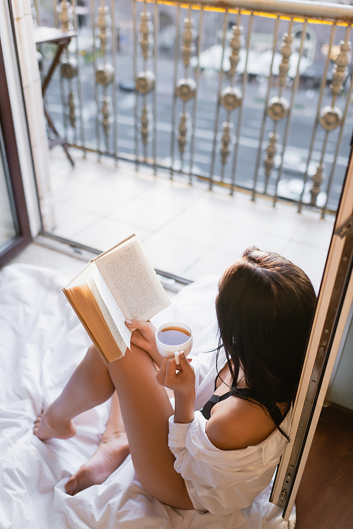 beautiful brunette woman in black underwear reading book and drinking tea sitting on blanket