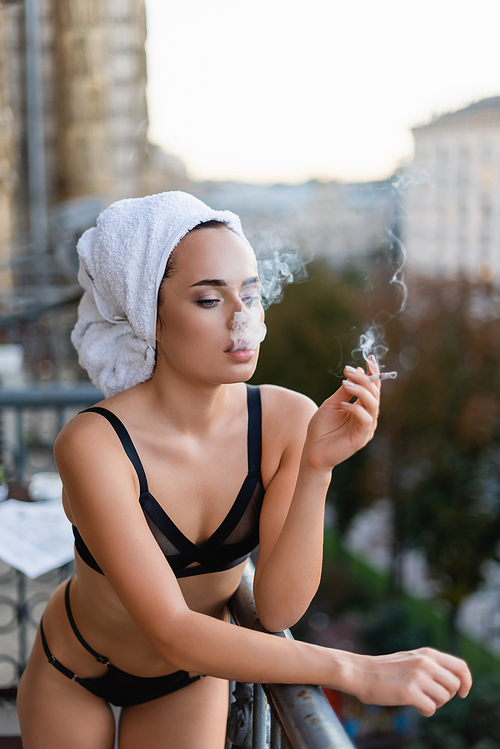sexy young woman in black underwear with towel on head smoking cigarette on balcony