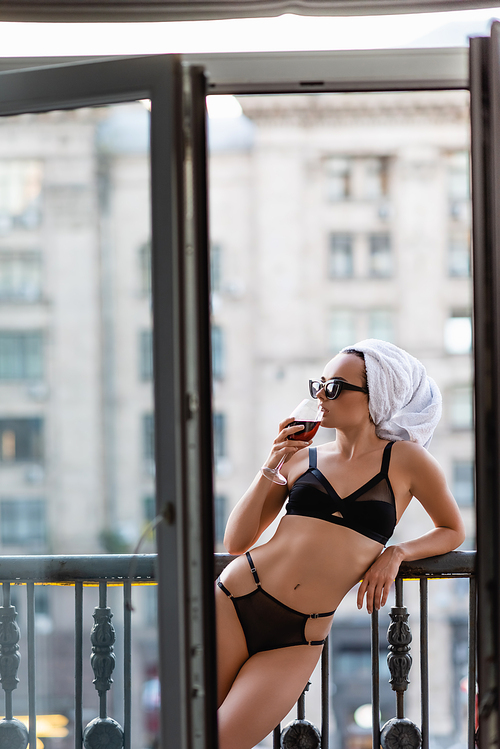 sexy young woman in black underwear with towel on head drinking red wine on balcony