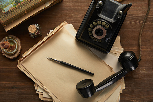 top view of vintage paper, painting, fountain pen, candle and dial phone on wooden table
