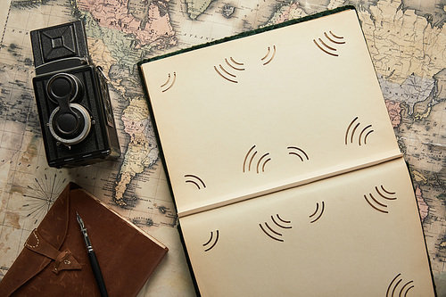 top view of vintage camera, notepad with fountain pen, empty photo album on map background