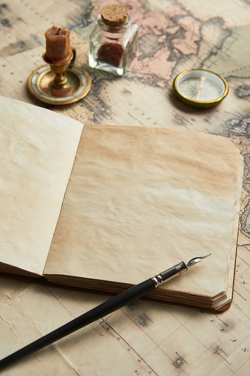 selective focus of vintage blank notebook with fountain pen near compass and candle on map background