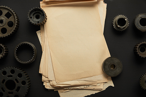 top view of aged gears and vintage blank paper on black surface