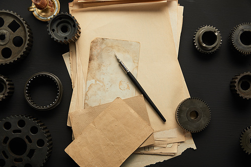 top view of aged gears and vintage blank paper with fountain pen on black surface