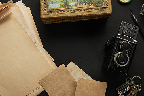 top view of vintage camera, paper, painting, fountain pen, keys on black background