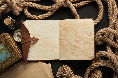 top view of vintage notebook, rope, compass and painting on black background