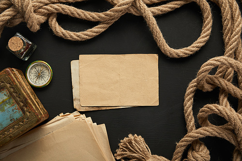 top view of vintage paper, rope, compass and painting on black background
