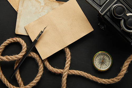 top view of vintage camera, paper, rope, fountain pen, compass on black background
