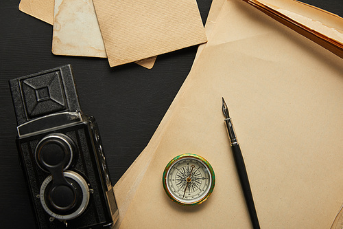 top view of vintage camera, paper, fountain pen, compass on black background