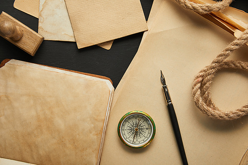 top view of vintage paper, rope, compass, stamp and fountain pen on black background