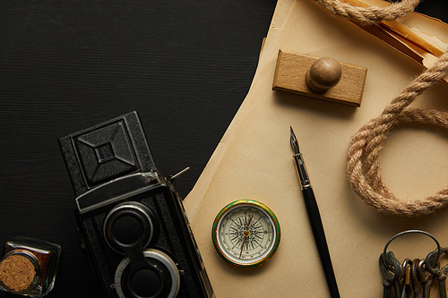 top view of vintage camera, paper, fountain pen, compass, stamp and keys on black background