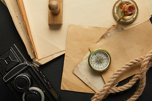 top view of vintage camera, paper, rope, compass, candle and stamp on black background