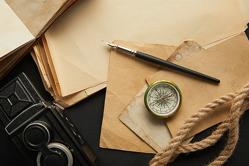 top view of vintage camera, paper, rope, compass and fountain pen on black background