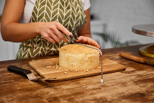 Partial view of confectioner cutting cake with cake slicer