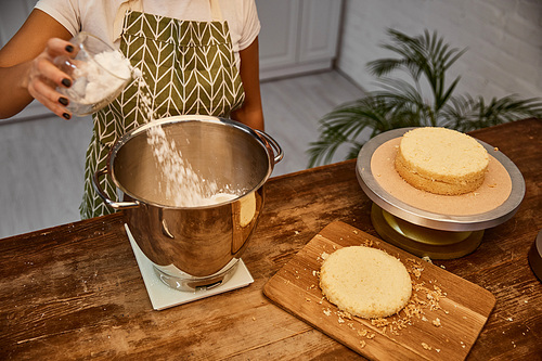 Cropped view of confectioner adding flour in bowl beside cake layers on table