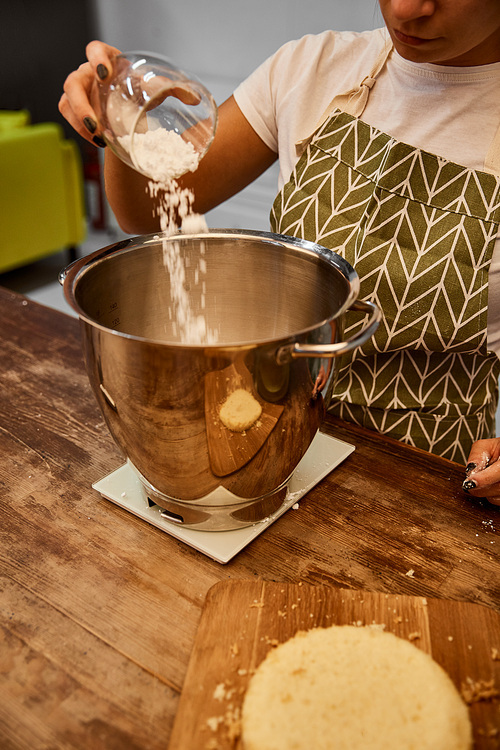 Cropped view of confectioner adding flour in bowl beside biscuit layer on cutting board