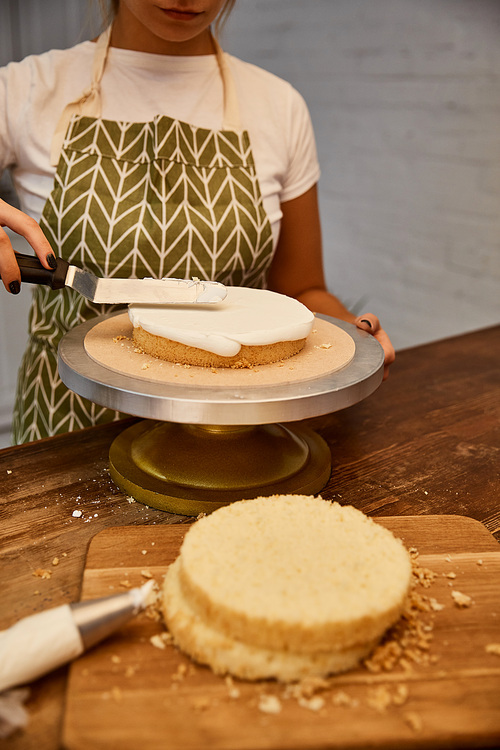 Cropped view of confectioner using spatula for sweet cream on cake layer