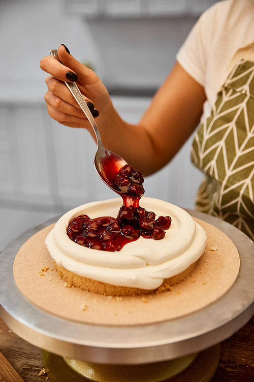 Cropped view of confectioner putting berry jam on cake layer with cream