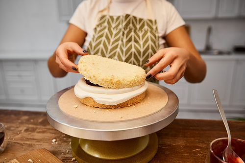 Cropped view of confectioner putting layer on sponge cake with cream
