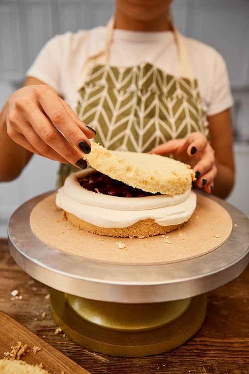 Cropped view of confectioner putting layer on biscuit with cream on stand
