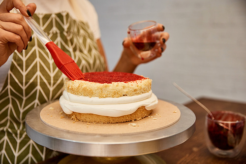 Cropped view of confectioner working with pastry brush and jam on biscuit