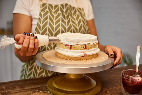 Cropped view of confectioner putting cream from pastry bag on sponge cake