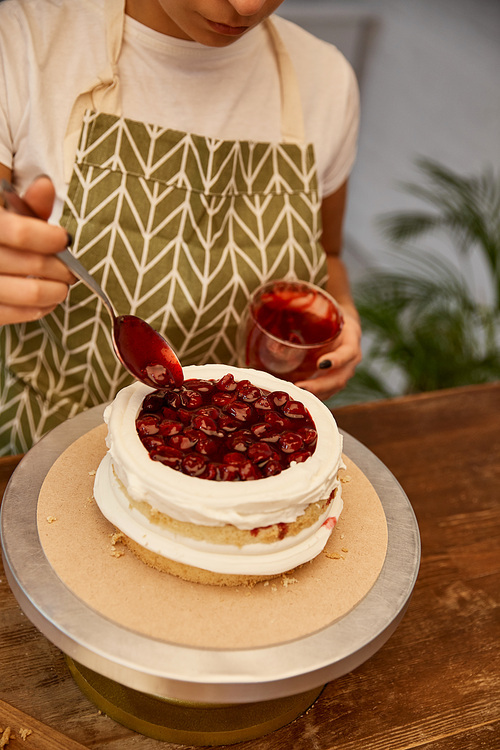 Copped view of confectioner adding tasty berry jam on cake layer