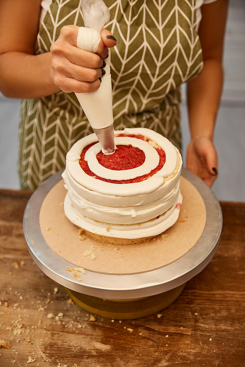 Cropped view of confectioner adding cream from pastry bag on cake