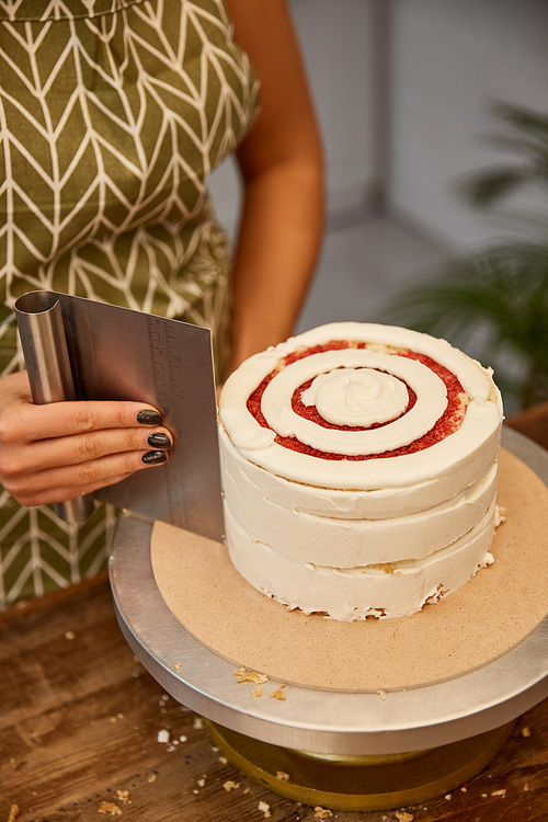 Cropped view of confectioner aligning cream with scraper on sponge cake