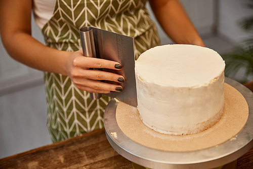 Cropped view of confectioner using scraper for cream on sponge cake