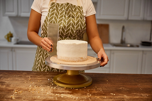 Cropped view of woman aligning cream on biscuit with scraper on stand