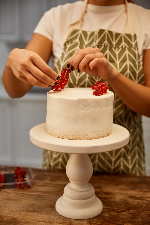 Cropped view of confectioner adding redcurrant on cake