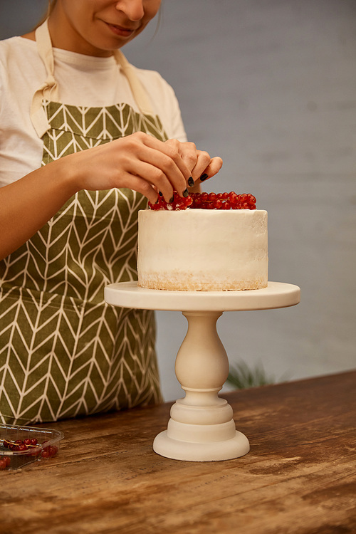 Cropped view of smiling confectioner decorating cake with sweet redcurrant